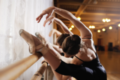 three young cute ballerinas perform exercises on a choreographic machine or barre on the background of a ballet class
